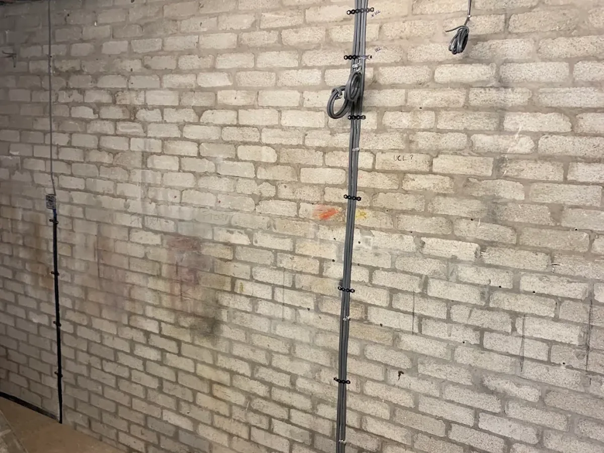 Steel conduit and cable containment installed on a brick wall during a rewire first fix